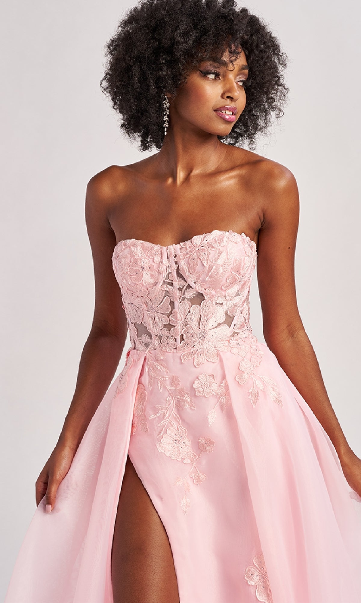 A woman models the Colette CL8660 long prom dress, featuring a strapless light pink design with an embroidered A-line skirt, sheer lace bodice, and high slit, set against a neutral background.